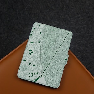 Op de afbeelding: Een rechthoekige, witte kaarthouder met een groen bladnervenpatroon en een kaartontwerp. De kaarthouder ligt op een bruin oppervlak, met een donkergrijze achtergrond.