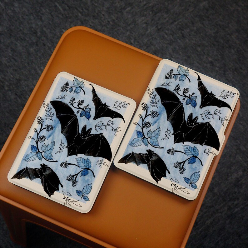 Puede incluir: Dos cubiertas de libro blancas con un dise&ntilde;o de murci&eacute;lago y zarzamora azul y negro. Las cubiertas son para un lector electr&oacute;nico Kindle.