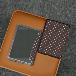 May include: A clear tablet case and a brown polka dot tablet cover are displayed on a brown surface. The tablet cover has a pattern of small, light pink dots. The tablet is visible inside the clear case.