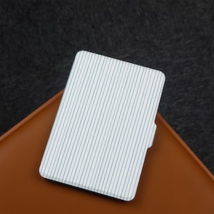 Puede incluir: Una funda a rayas blancas y azul claro, posiblemente para un tel&eacute;fono o tableta, descansa sobre una superficie marr&oacute;n. La funda tiene un patr&oacute;n de rayas verticales y un borde curvo. El fondo es de color gris oscuro.