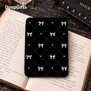 May include: A black e-reader cover featuring a white diamond grid pattern with small white bows at each intersection. The cover has a smooth, matte finish and is rectangular with rounded corners, displaying a consistent repeating design.