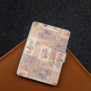 Könnte beinhalten: Eine Tablet-Hülle mit floralem Patchwork-Design. Die Hülle weist eine Vielzahl von Pastellfarben auf, darunter Rosa, Lavendel und Creme, mit floralen und karierten Mustern. Die Hülle ist rechteckig mit einem Magnetverschluss.