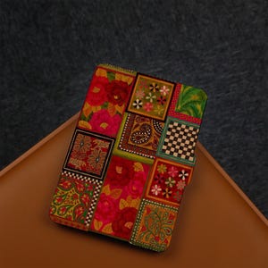 Pode incluir: Uma capa para leitor de e-books com um design de patchwork colorido com uma variedade de padrões florais e geométricos em tons de vermelho, verde, amarelo e azul.