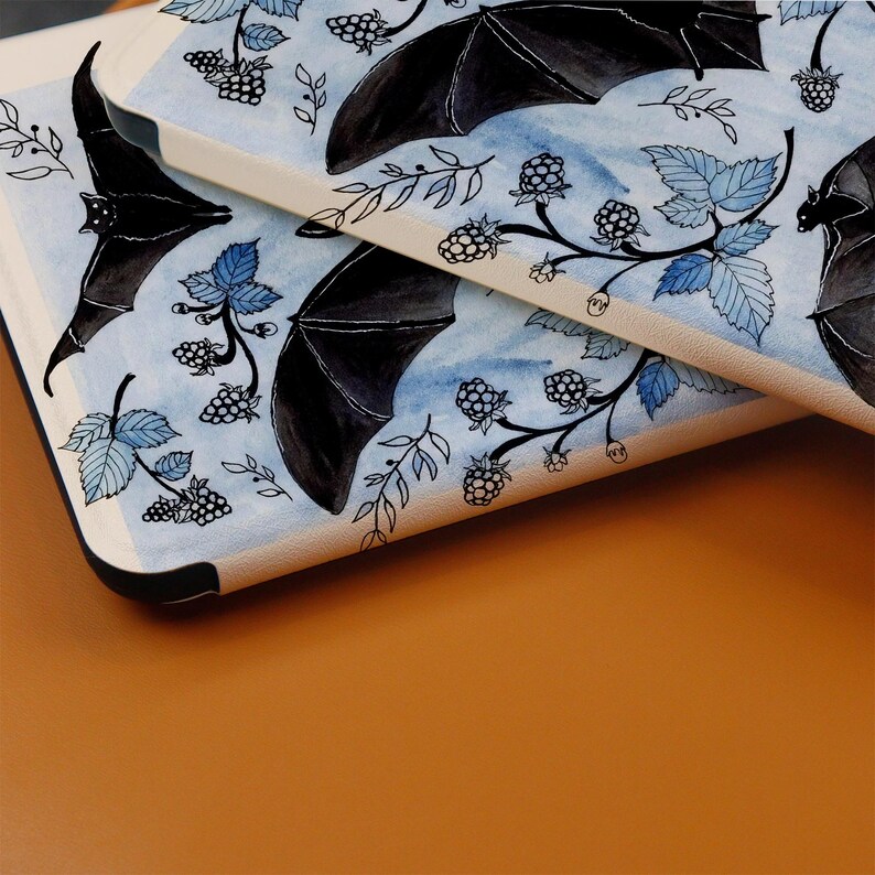 Puede incluir: Una funda de tel&eacute;fono blanca con un dise&ntilde;o de acuarela azul y negro con murci&eacute;lagos y moras. El dise&ntilde;o se repite en la parte posterior de la funda.