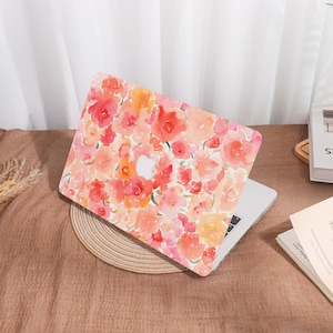 May include: A laptop computer with a floral patterned cover. The cover features a watercolor design of red, pink, and orange flowers on a white background. The laptop is on a brown surface.