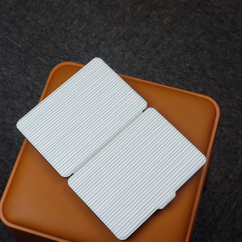 Puede incluir: Dos objetos rectangulares blancos con un patr&oacute;n de rayas azul claro se muestran sobre una superficie de cuero marr&oacute;n. Los objetos est&aacute;n ligeramente abiertos, revelando un vistazo del interior. El fondo es una superficie gris oscuro y texturizada.