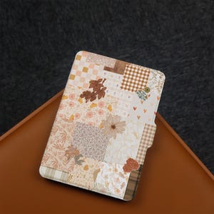 May include: A tablet case with a patchwork design. It features floral, gingham, and solid fabric squares in beige, brown, and cream. The case has a tab closure and is set on a brown surface.