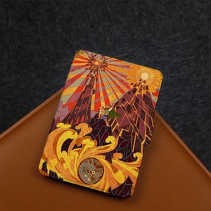 May include: A colorful, decorative case featuring a stained-glass style illustration. The design includes a mountain scene with a figure in a green cape, a sunburst, and ornate, swirling patterns in shades of yellow, orange, and brown.