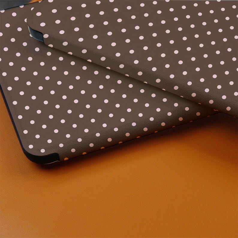 May include: Close-up of two brown cases with a repeating pattern of small, white polka dots. The cases have black edges and are slightly overlapping, creating a layered effect. The background is a solid, warm orange color.