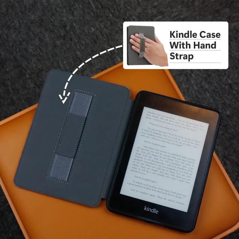 May include: A black Kindle e-reader with a gray case featuring a hand strap. The Kindle is open, displaying text on the screen. The case is open, revealing a stand. The text "Kindle Case With Hand Strap" is in the upper right corner.
