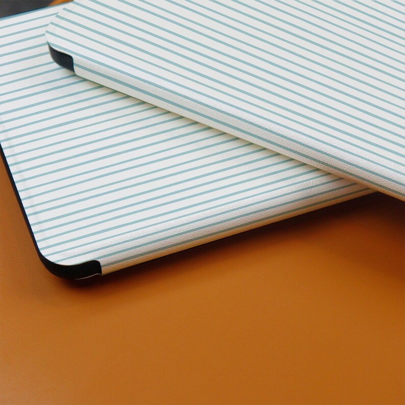 Puede incluir: Dos objetos rectangulares con esquinas redondeadas est&aacute;n apilados. El objeto superior tiene un fondo blanco con finas rayas horizontales de color azul claro. El objeto inferior es parcialmente visible, con una superficie marr&oacute;n oscuro s&oacute;lida. Los bordes de los objetos son negros.
