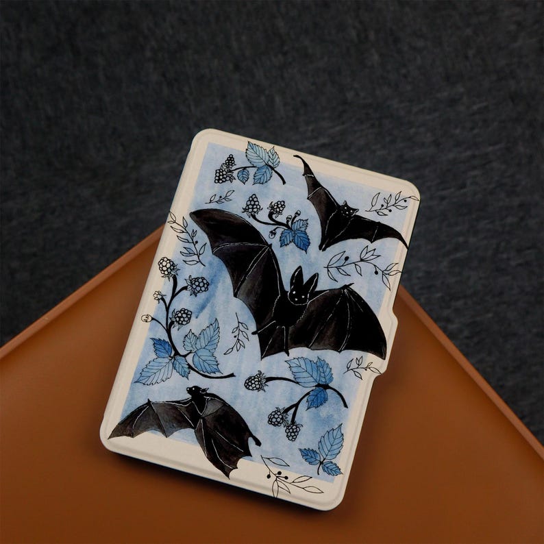 Puede incluir: Una funda blanca para lector electr&oacute;nico con un fondo azul acuarela con murci&eacute;lagos negros y moras.