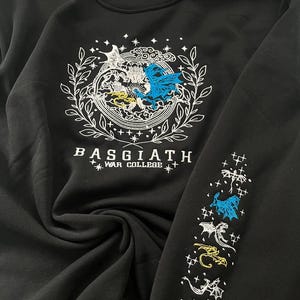 May include: Black sweatshirt with a white embroidered design featuring two dragons and the text "BASGIATH WAR COLLEGE". The right sleeve has a repeating pattern of embroidered dragons.