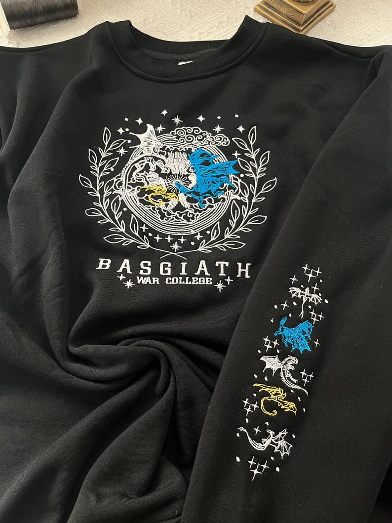 May include: Black sweatshirt with a white embroidered design featuring two dragons and the text "BASGIATH WAR COLLEGE". The right sleeve has a repeating pattern of embroidered dragons.