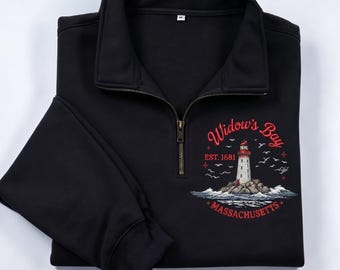 May include: A black quarter-zip sweatshirt featuring a graphic of a lighthouse on a rocky island with the text Widow's Bay EST. 1681 MASSACHUSETTS in red lettering. The design includes flying birds and crashing waves around the lighthouse base.