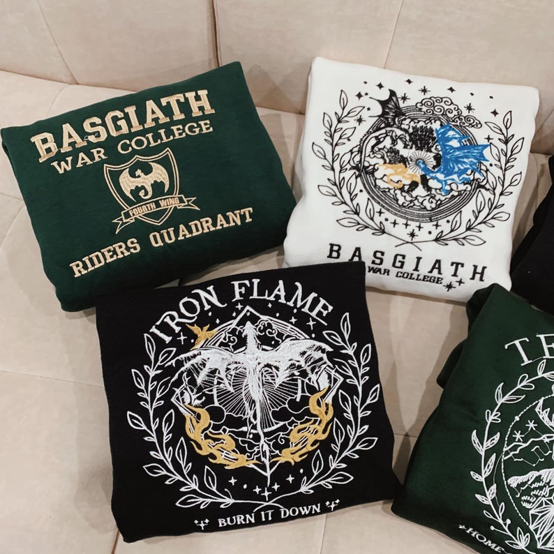 May include: Four green, black, and white sweatshirts with embroidered designs. The designs feature dragons, flames, and the text "BASGIATH WAR COLLEGE", "FOURTH WING", "RIDERS QUADRANT", "IRON FLAME", and "BURN IT DOWN".