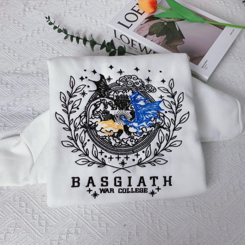 May include: White sweatshirt with black embroidered design of two dragons, clouds, and stars. The text "BASGIATH WAR COLLEGE" is embroidered below the design.