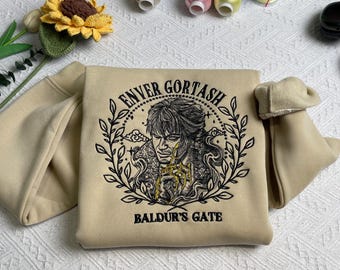 Op de afbeelding: Een beige sweatshirt met een zwart geborduurd ontwerp met een portret van een personage, de tekst "Enver Gortash" en de woorden "Baldur's Gate".