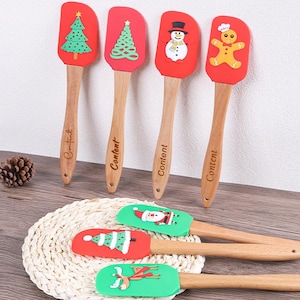 May include: A collection of Christmas-themed spatulas with wooden handles and red or green silicone heads. The spatulas feature festive designs like Christmas trees, a snowman, a gingerbread man, Santa Claus, and reindeer. The word "Content" is printed on the wooden handles.