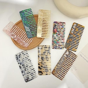 Op de afbeelding: Een verzameling kleurrijke haar kammen in verschillende patronen en ontwerpen. De kammen zijn gemaakt van een gemarmerd materiaal in roze, groen, beige en veelkleurige tinten. Sommige kammen hebben de tekst "JACOB", "Engraving" en "TW".