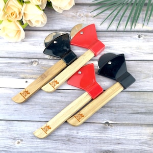 Puede incluir: Cuatro cortadores de pizza con forma de hacha. Dos tienen cabezas de hacha negras y dos rojas. Los mangos son de bambú y tienen un logotipo impreso. Los cortadores de pizza están colocados sobre una superficie de madera.