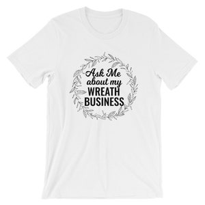 Peut inclure: T-shirt blanc avec un motif de couronne noire et le texte "Ask Me about my WREATH BUSINESS".
