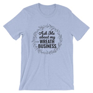 Peut inclure: T-shirt bleu clair avec un graphique noir d'une couronne avec le texte "Ask Me about my Wreath Business".