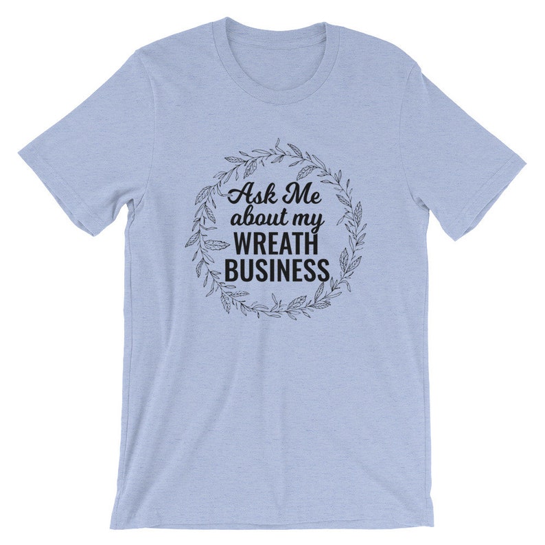 Peut inclure: T-shirt bleu clair avec un graphique noir d'une couronne avec le texte "Ask Me about my Wreath Business".