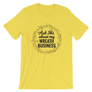 Peut inclure: T-shirt jaune avec un motif de couronne noire et le texte "Ask Me about my Wreath Business".