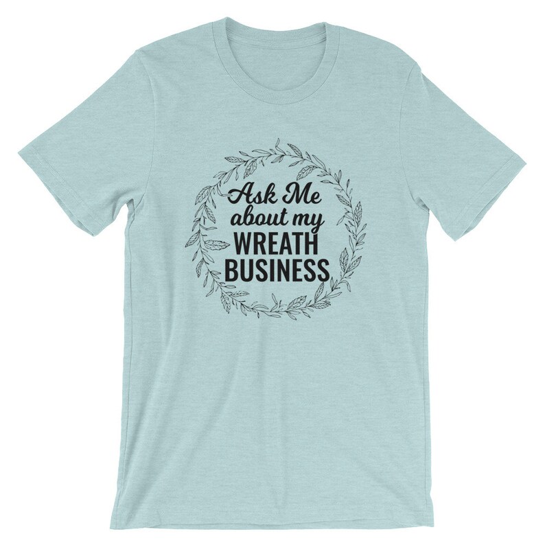 Peut inclure: Un t-shirt bleu clair avec le texte "Ask Me about my Wreath Business" &agrave; l'int&eacute;rieur d'une couronne.