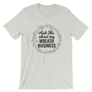 Peut inclure: Un t-shirt gris chin&eacute; avec le texte "Ask Me about my Wreath Business" &agrave; l'int&eacute;rieur d'une couronne.