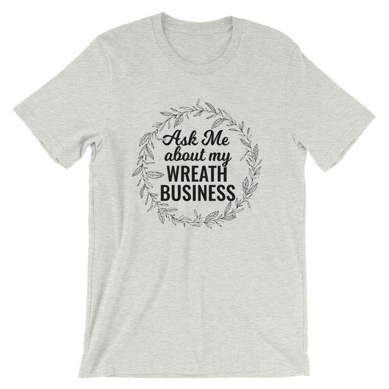 Peut inclure: Un t-shirt gris chin&eacute; avec le texte "Ask Me about my Wreath Business" &agrave; l'int&eacute;rieur d'une couronne.