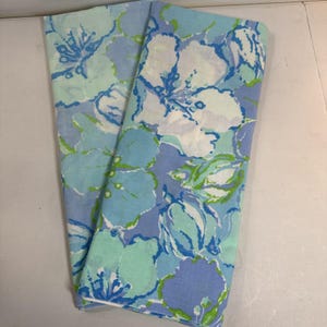 May include: Folded fabric with a floral pattern in shades of blue, white, and green. The design features large, stylized flowers and leaves. The fabric appears to be lightweight and suitable for various applications.