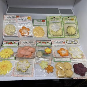 May include: A collection of packaged silk flower petals in various colors, including ivory, orange, yellow, peach, and white. The packages are labeled with the brand names "Pretty Petals" and "Posies".