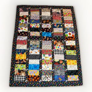 May include: A patchwork quilt with a black border featuring colorful polka dots. The quilt's interior is composed of numerous rectangular fabric patches in various patterns, including florals, sports balls, and geometric designs. The quilt is rectangular and appears to be handmade.
