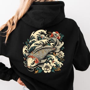 May include: Black hooded sweatshirt featuring a detailed illustration of a koi fish swimming through waves, with floral accents. The design includes shades of white, red, and gold. The sweatshirt has a drawstring hood and a kangaroo pocket.