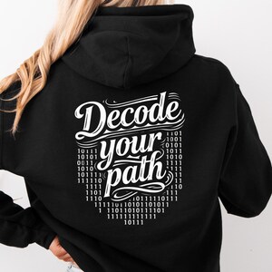 Könnte beinhalten: Schwarzer Kapuzenpullover mit dem weißen Text "Decode your path". Das Design enthält Binärcode in Herzform. Der Hoodie hat eine Kapuze und lange Ärmel.