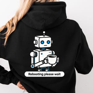 Può includere: Felpa con cappuccio nera con un disegno di robot bianco e blu che tiene una tazza di caffè. Il robot ha occhi blu e una piccola antenna. Il testo "Rebooting please wait" è sotto.