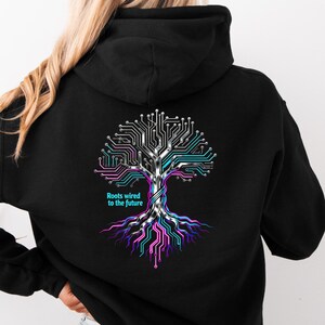 Könnte beinhalten: Schwarzer Kapuzenpullover mit einem Baumdesign aus Leiterplattenlinien in Silber, Türkis, Pink und Lila. Der Text "Roots wired to the future" steht unter dem Baum. Der Hoodie hat eine Kapuze und eine Vordertasche.