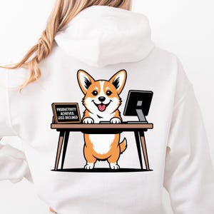 Pode incluir: Moletom branco com um desenho de cachorro corgi de desenho animado. O corgi é retratado em uma mesa com um computador, com o texto "PRODUTIVIDADE ALCANÇADA. PERNAS DECLINADAS" em um pequeno sinal. O corgi é laranja e branco.