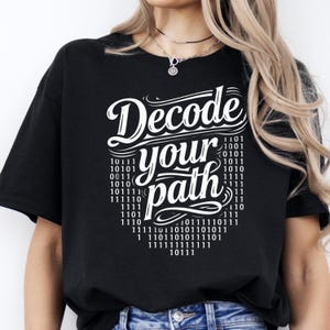 Op de afbeelding: Zwart t-shirt met de witte tekst "Decode your path". Het ontwerp bevat binaire code rond de tekst. Een casual t-shirt voor liefhebbers van coderen of technologie.