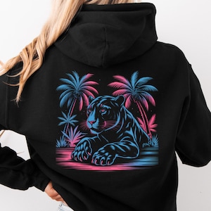 Peut inclure: Sweat à capuche noir avec un motif néon d'une panthère et de palmiers. La panthère est couchée, avec des contours bleus et roses. Les palmiers sont également bleus et roses. Le sweat à capuche a une capuche et des manches longues.
