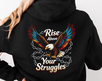 May include: Black hoodie featuring a colorful eagle graphic with outstretched wings and the words "Rise Above Your Struggles." The eagle has brown, blue, red, and yellow feathers, and is surrounded by chains.