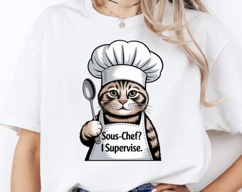 Puede incluir: Camiseta blanca con un gato de dibujos animados con gorro y delantal de chef, sosteniendo una cuchara. El delantal dice "Sous-Chef? I Supervise." El gato tiene pelaje marrón y beige. La camiseta es de estilo casual.