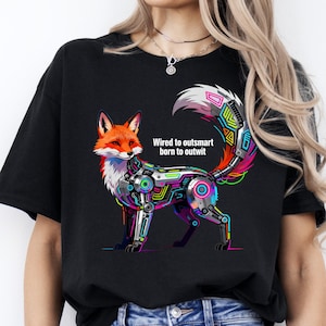 Op de afbeelding: Zwart t-shirt met een gestileerd vossendesign. De vos combineert natuurlijke en robotachtige elementen met neonaccenten. De tekst "Wired to outsmart born to outwit" is zichtbaar.