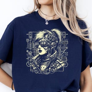 May include: Navy blue t-shirt featuring a futuristic woman with cybernetic enhancements. The illustration is in a detailed, technical style with a network of lines and circuits. The woman wears futuristic glasses and has a high ponytail.