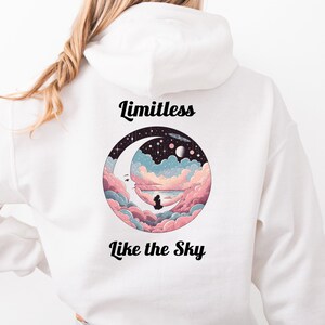 May include: White hoodie with a circular graphic on the back featuring a night sky, moon, and clouds in shades of pink, blue, and purple. The words "Limitless" and "Like the Sky" are printed above and below the graphic in black.