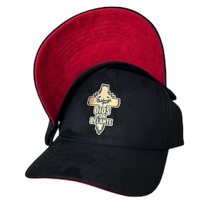 Op de afbeelding: Zwarte baseballpet met een rode onderkant. De pet heeft een gouden kruisontwerp met de woorden "DIOS POR DELANTE" in gouden letters. De pet heeft een gebogen klep en een gestructureerde kroon.