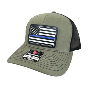May include: Olive green and black trucker hat with a patch featuring a US flag with a blue stripe. The hat has a curved brim and a mesh back. The patch reads "RICHARDSON ORIGINAL 112 TRUCKER ADJUSTABLE".