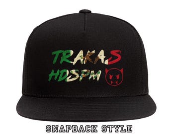 May include: Black snapback style hat with the text "TRAKAS HDSPM" in green, white, and red lettering with a red devil face graphic.